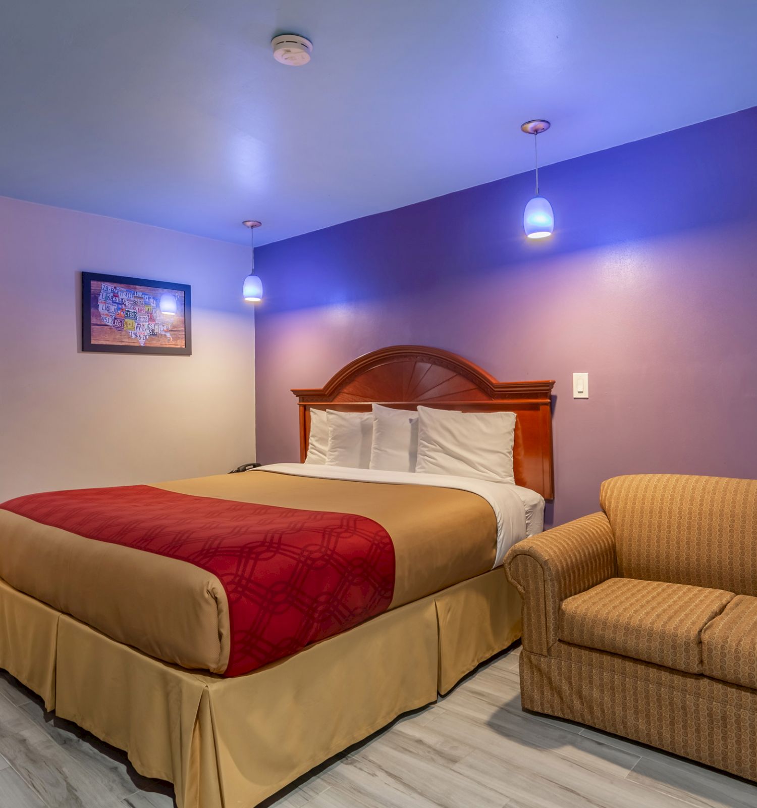 A hotel room with a bed, red bedspread, a framed picture, a couch, and blue walls with a bathroom in the background.